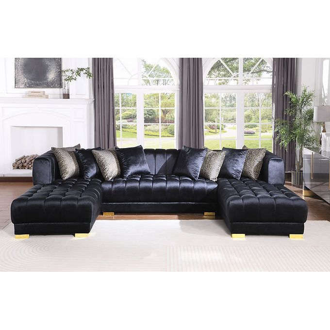 Black velvet sectional sofa with gold legs and accent pillows in a living room