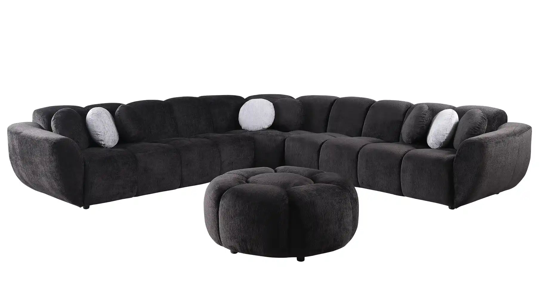 Black modular sectional sofa with channel-stitched cushions, round bolster pillows, and matching round ottoman in a modern living room