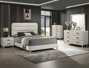 Nyomi upholstered bed with channel-tufted headboard and matching light wood-tone dresser, mirror, chest, and nightstand in a modern bedroom