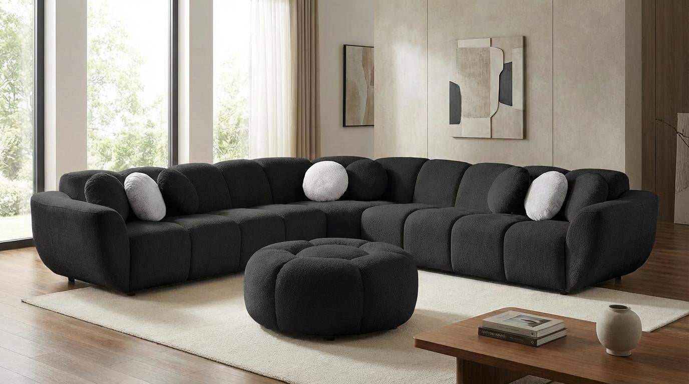Black modular sectional sofa with channel-stitched cushions, round bolster pillows, and matching round ottoman in a modern living room